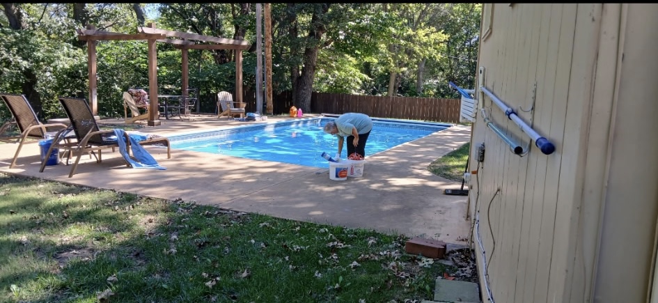Backyard pool after cleaning, clear blue water with pergola and deck chairs