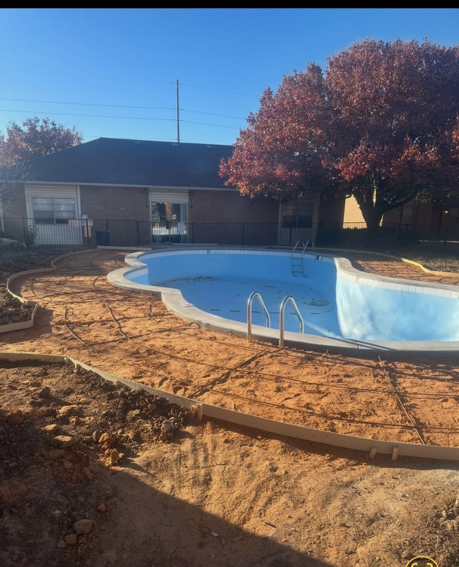 Kidney-shaped pool before renovation, drained with dirt deck under construction